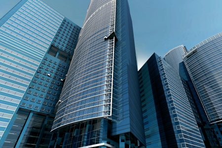 Futuristic urban skyscrapers with glass facades reflecting a vibrant blue sky.